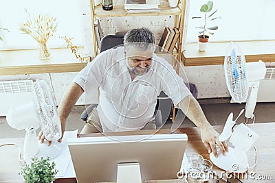 Businessman, manager in office with computer and fan cooling off, feeling hot, flushed Stock Photo