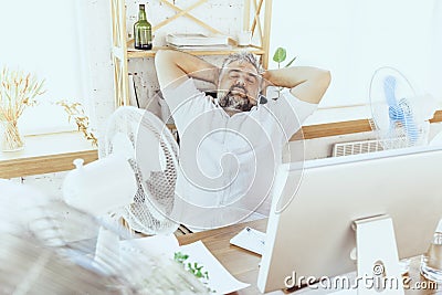 Businessman, manager in office with computer and fan cooling off, feeling hot, flushed Stock Photo