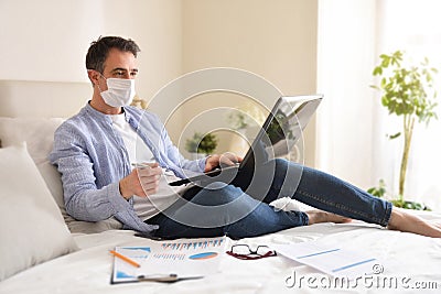 Businessman with mask working with laptop lying on a bed Stock Photo