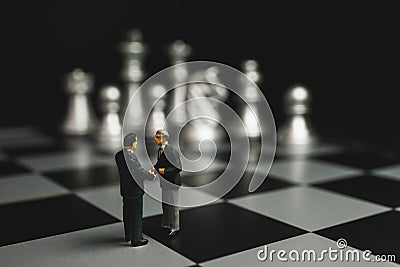 Businessman miniature handshake on chessboard with silver chess background. Stock Photo