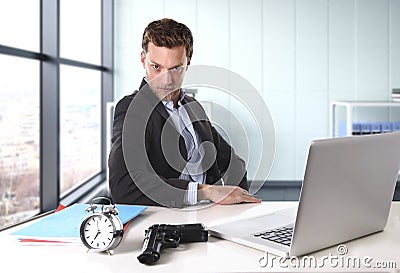 Businessman at office computer desk posing with gun and alarm clock in deadline concept Stock Photo