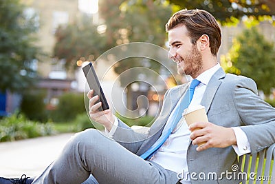 Businessman On Park Bench With Coffee Using Digital Tablet Stock Photo