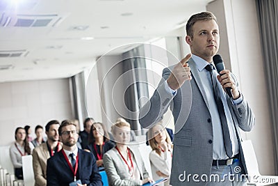 Businessman pointing while speaking through microphone during seminar in convention center Stock Photo