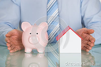 Businessman Protecting Piggy Bank And House Model Stock Photo