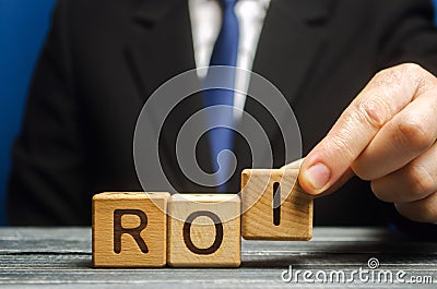 Businessman puts wooden blocks with the word ROI. Return on investment concept. Profitability and loss-making of investments. ROMI Stock Photo
