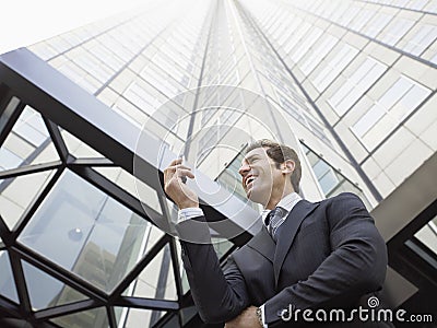 Businessman Reading SMS On Mobile Phone Against Office Building Stock Photo