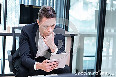 A businessman reads information about the investment inside the tablet he is holding. Stock Photo