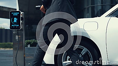 Businessman recharge his electric car from charging station. Peruse Stock Photo