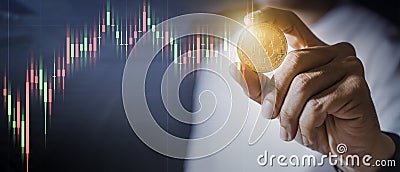 Businessman`s hand holds the floating gold Bitcoin which is virtual money on a with a backdrop of the falling stock graph. Make m Stock Photo