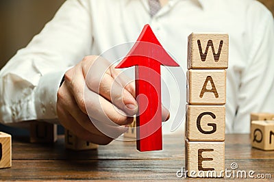 Businessman`s hand holds red arrow up near wooden blocks with word Wage. Salary increase concept. Wages rate. Revenue growth and Stock Photo