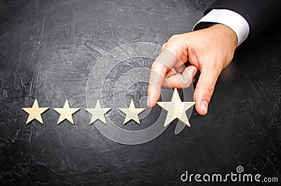 The businessman`s hand in the suit holds the fifth star. Get the fifth star. The concept of the rating of hotels and restaurants, Stock Photo