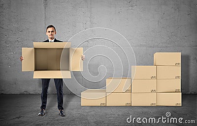 Businessman is showing an open box in his hands staying on gray background Stock Photo