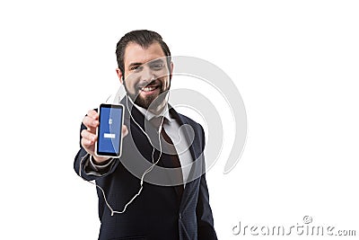 Bearded businessman with earphones showing smartphone with facebook website Editorial Stock Photo