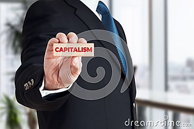 Businessman shows a wooden block with the word capitalism. Global corporate capitalism Stock Photo