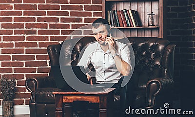 A businessman sits on the couch and calls from the phone. Rich man is surrounded by a stylish interior of the room Stock Photo