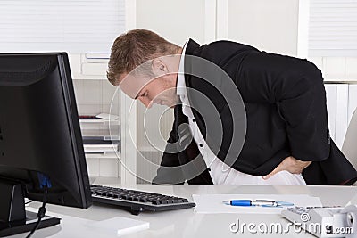 Businessman sitting at desk having pain at back, kidneys or muscles. Stock Photo