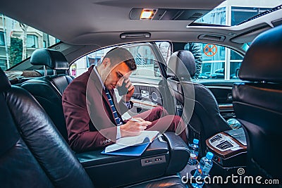 Businessman sitting in a limo while talking on his phone reading his notes and planning his day Stock Photo