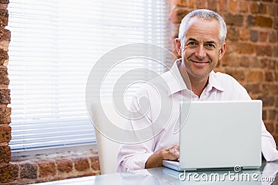 Businessman sitting in office on laptop smiling Stock Photo