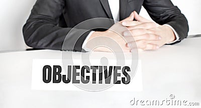 Businessman sitting at the table and signboard with text OBJECTIVES Stock Photo