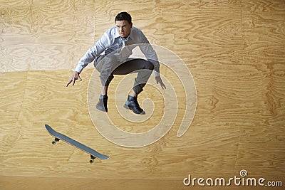 Businessman With Skateboard Jumping Against Wood Paneling Stock Photo