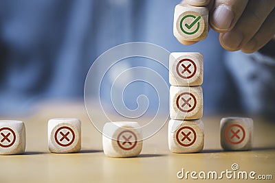 Businessman stacking green correct sign mark on top of Red Cross mark which print screen on wooden cube block for approve and Stock Photo