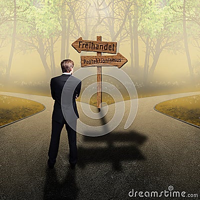 Businessman standing at crossroad having to decide between `free trade` and `protectionism` with road signs in German Stock Photo