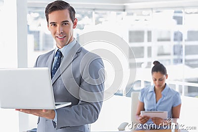 Businessman standing with laptop and smiling at camera Stock Photo