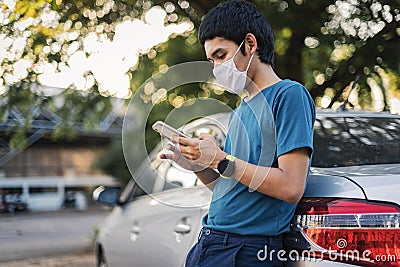 Businessman standing on the car and check mobile phone for business. Wearing a face mask to protect against coronavirus Stock Photo