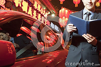 Businessman standing next to his car at night reading, Red lanterns in the background Stock Photo