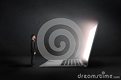 Businessman stands front of an open glowing huge laptop in the darkness. Profile view. Stock Photo