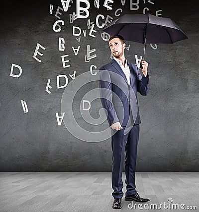 Businessman stands with umbrella under falling letters. Stock Photo