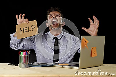 Businessman in stress working at office computer desk holding sign asking for help screaming crazy Stock Photo