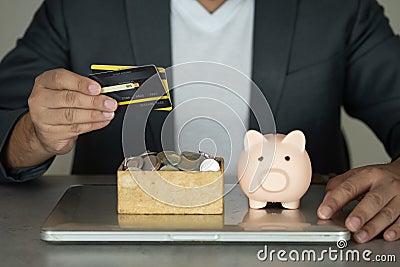 Businessman in suit holding credit card and pink piggy bank with stock of coin in box place on notebook Stock Photo