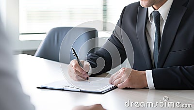 Businessman in suit signing a contract or agreement with another businessman in the background Stock Photo
