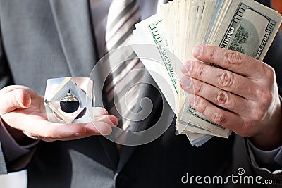 Businessman in suit, tie holds in hands drop of black oil of Brent brand in crystal cube.Pack of hundred dollars bills.Crisis in Stock Photo