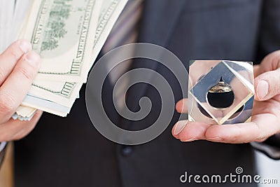 Businessman in suit, tie holds in hands drop of black oil of Brent brand in crystal cube.Pack of hundred dollars bills.Crisis in Stock Photo