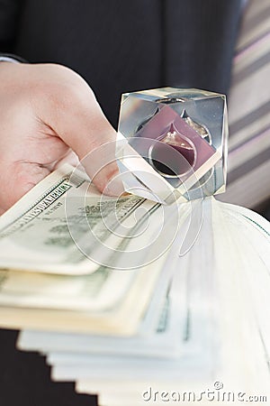 Businessman in suit, tie holds in hands drop of black oil of Brent brand in crystal cube.Pack of hundred dollars bills.Crisis in Stock Photo