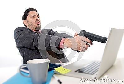 Businessman in suit and tie sitting at office desk working on computer pointing gun to laptop in business problems and stress Stock Photo