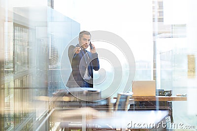 Businessman talking on a mobile phone in corporate office, pointing to camera. Stock Photo