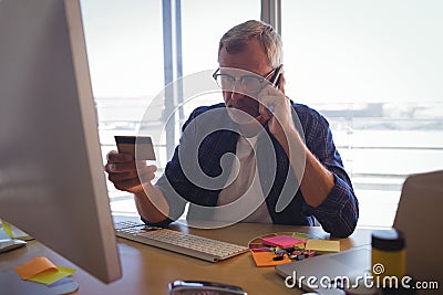 Businessman talking on mobile phone while holding credit card at office Stock Photo