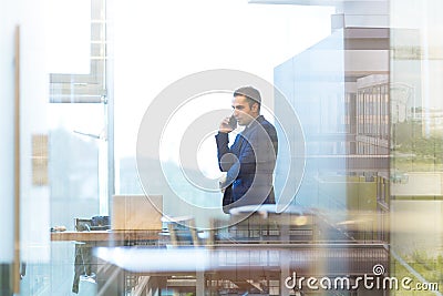 Businessman talking on a mobile phone while looking through office window. Stock Photo