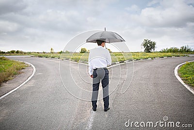 Businessman with umbrella standing at crossroads. Concept of choice Stock Photo
