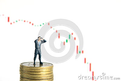 Businessman using binoculars standing above coin stack, with falling candle stick chart. Miniature tiny people toys photography. Stock Photo