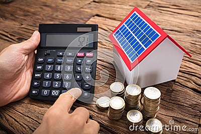 Businessman Using Calculator By Coins And Solar Model Home Stock Photo