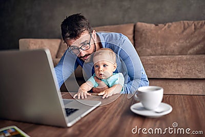 Businessman using a laptop computer for work at home while looking after his baby son. Stock Photo