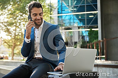 Businessman using a laptop outside and talking on his cellphone Stock Photo