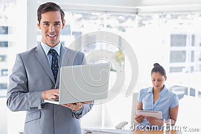 Businessman using laptop standing in office smiling at camera Stock Photo