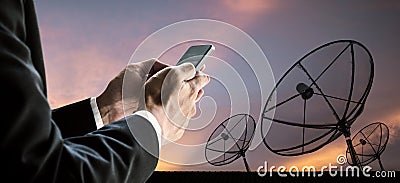 Businessman using smart phone, with silhouette telecoms satellite dish digital network and sunset sky Stock Photo