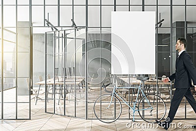 Businessman walking in modern glass partition and bike in stylish coworking office interior with empty white mock up poster and Stock Photo