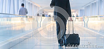 Businessman walking and wheeling a trolley suitcase at the lobby, talking on a mobile phone. Business travel concept. Stock Photo